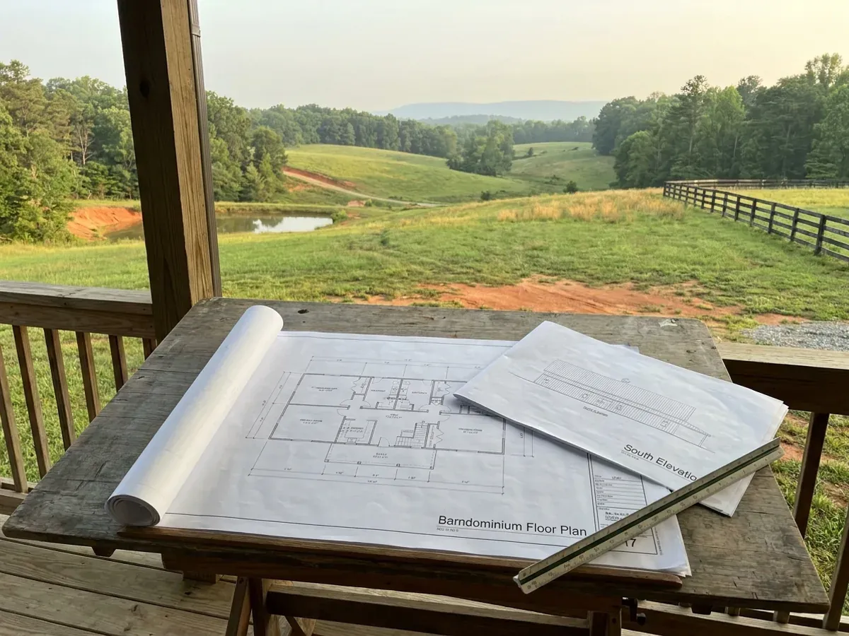 Barndominium floor plan and elevation drawings laid out on a drafting table with a scale rule.