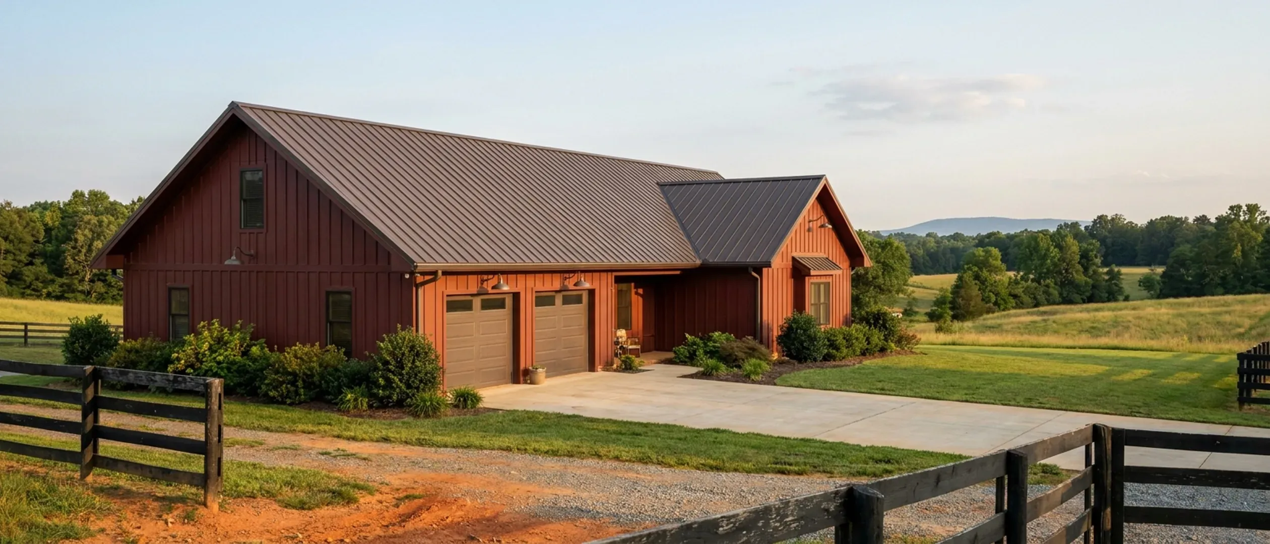 A completed barndominium viewed from a low angle showing its standing seam metal roof, vertical wall panels, gutters and exterior wall lights.