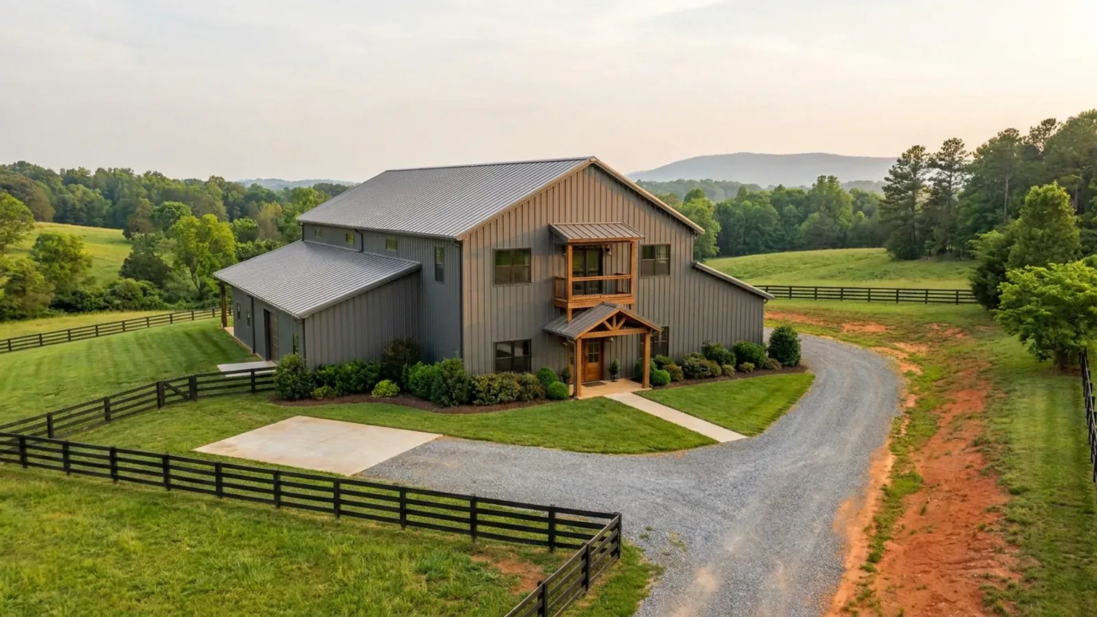A completed two-story barndominium with visible second-story windows and a small covered balcony above the entry porch.